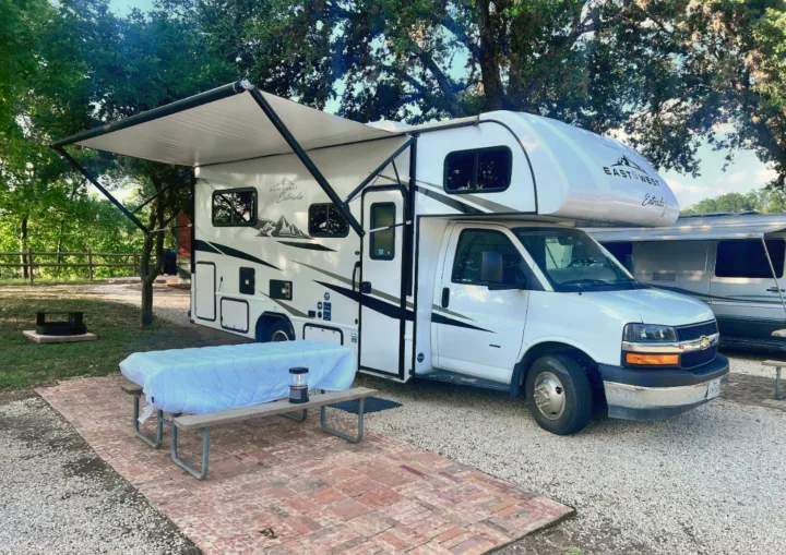 White RV rental at a scenic campsite with an extended awning and picnic table. Perfect for camping adventures.. East to West Entrada 2026