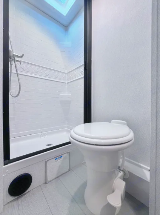 Compact RV rental bathroom showcasing a clean white shower with a skylight and a modern toilet, ready for your travels.. East to West Entrada 2026