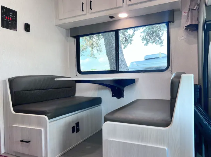 Cozy RV rental dinette featuring dark cushioned benches, a wall table, and window view. Ideal for travel or camping.. East to West Entrada 2026