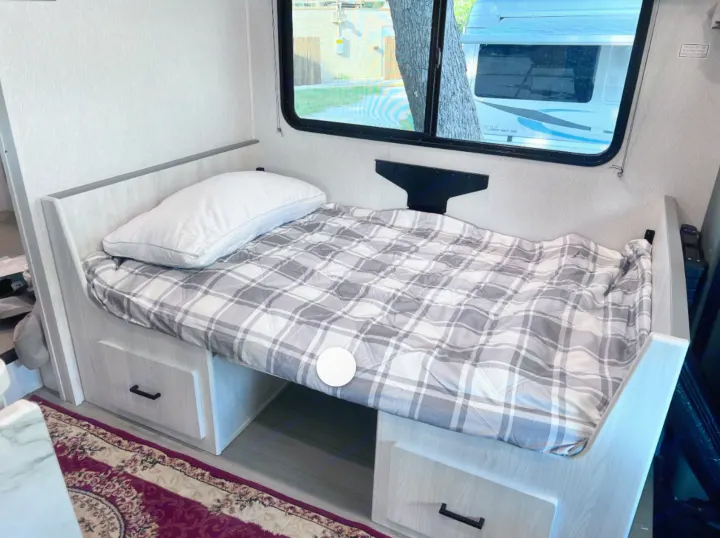 RV rental interior: cozy bed with plaid comforter, pillow, and built-in storage drawers beneath.. East to West Entrada 2026
