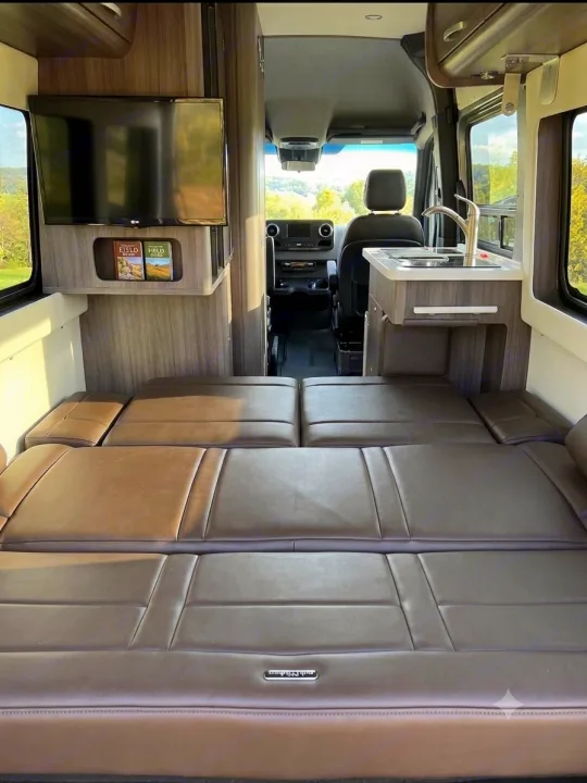 This RV rental interior offers a comfortable bed, TV, and kitchenette, ideal for travel and adventures.. Airstream Interstate 2022