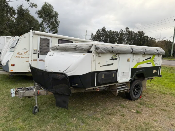 A Jayco pop-top camper trailer (RV rental option) and a caravan parked on grass. Cloudy sky and trees in the background.. Outback Eagle Off-Road 2015
