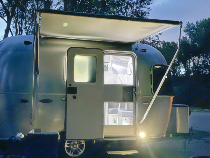 Illuminated silver travel trailer (RV rental) with an open door and extended awning at night, offering a cozy camping view.. Airstream Sport 2019