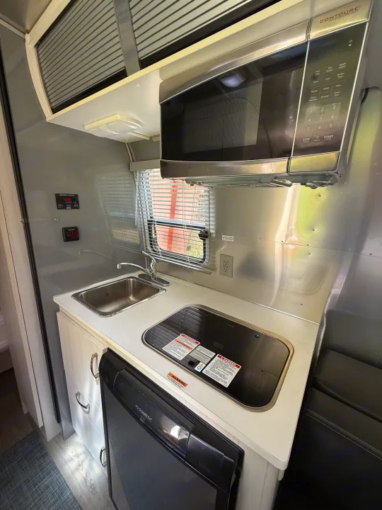 Compact rv rental kitchen: microwave, sink, stovetop, and Dometic fridge in a sleek camper interior.. Airstream Sport 2019