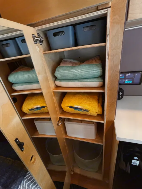 RV rental: Organized wooden cabinet storage with bins, striped blankets, and yellow towels. Compact living essentials.. Ford Transit 2021