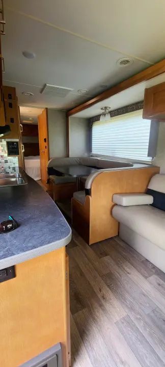 Inside a comfortable rv rental: modern kitchen, dining booth, sofa, and a glimpse of the bedroom. Wood-look flooring.. Winnebago Minnie Winnie 2019