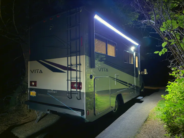 This Winnebago Vita RV rental is brightly lit at night with awning lights, parked for an outdoor journey or camping.. Winnebago Vita 2020