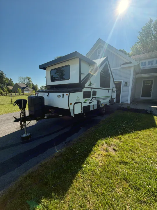 Sunny day with a white pop-up RV rental parked in a driveway next to a house, ready for your next adventure!. Forest River Rockwood Premier 2021