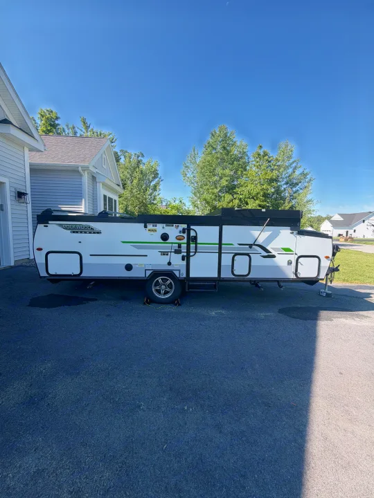 A Rockwood High Wall pop-up rv rental is parked on asphalt beside a house, ready for your next travel adventure under a sunny sky.. Forest River Rockwood Premier 2021