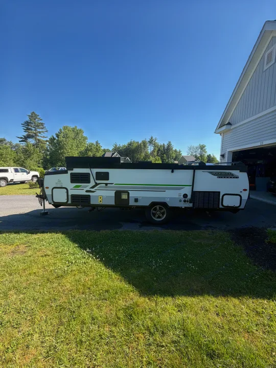 A white and grey Rockwood High Wall A-frame camper, an RV rental, parked on a driveway near a house on a sunny day.. Forest River Rockwood Premier 2021