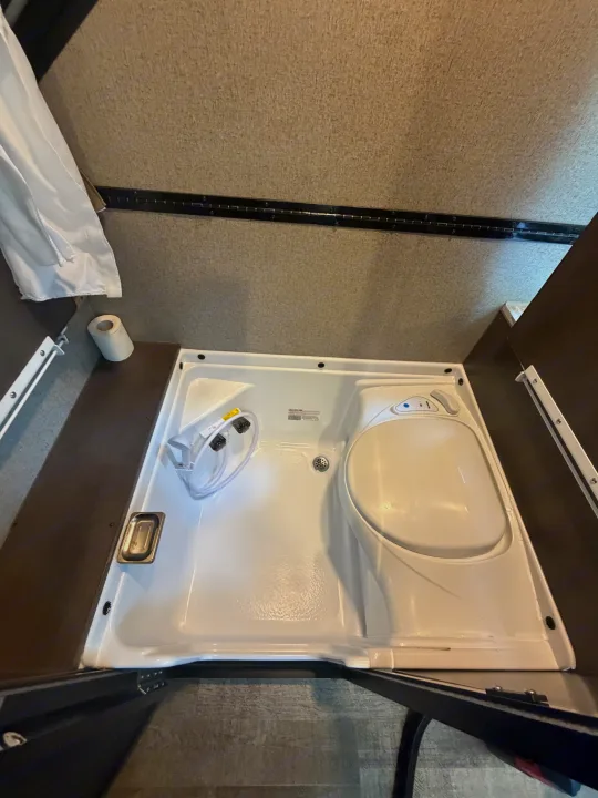 This RV rental's compact wet bath features an integrated toilet and shower head, designed for space-saving. Toilet paper is on a shelf.. Forest River Rockwood Premier 2021