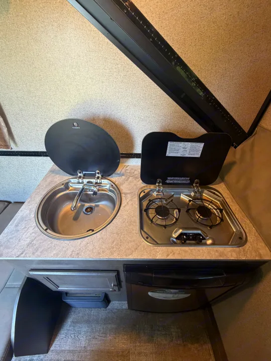 Compact RV rental kitchen featuring a Dometic sink and two-burner gas stove on a marbled counter.. Forest River Rockwood Premier 2021