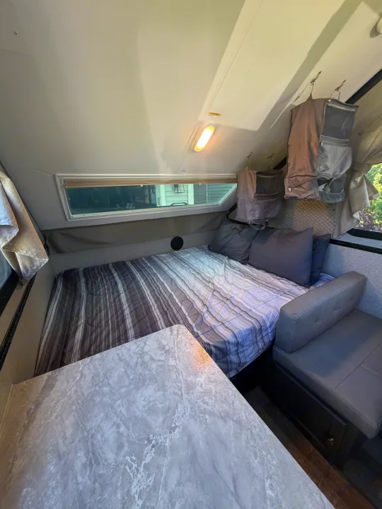 Cozy RV rental interior featuring a striped bed, marble-top dinette, bench seating, and hanging storage. Ideal for road trips.. Forest River Rockwood Premier 2021