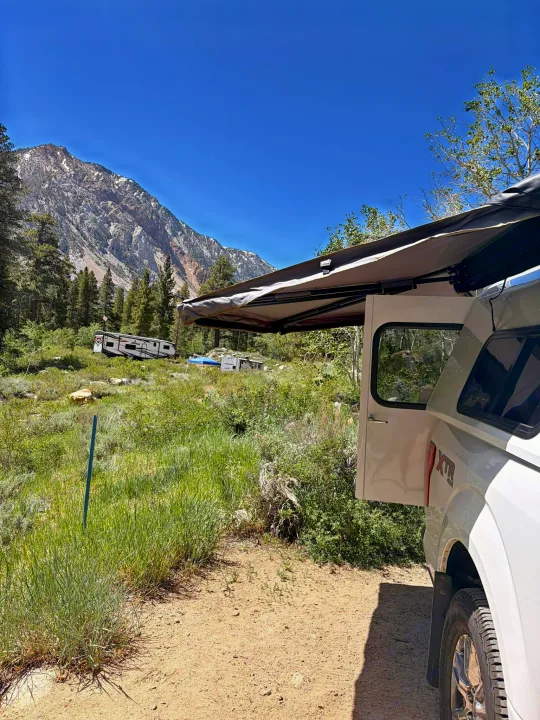 Mountain camping adventure! White truck, awning extended. RVs in the distance suggest an ideal rv rental destination. Clear skies, great outdoors.. Ford Ford F150 2017