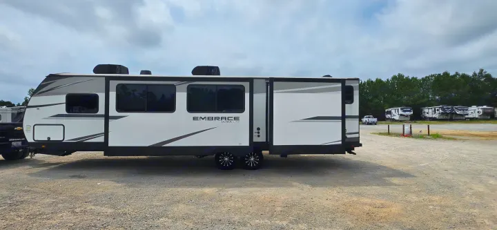 White & grey Embrace Ultra-Lite travel trailer RV rental, slide-out extended, parked on a gravel lot with other RVs.. Cruiser RV 2024