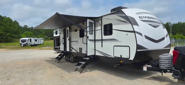 An Embrace Ultra-Lite RV rental, with awning extended and steps down, is hitched for travel. Another RV is visible nearby.. Cruiser RV 2024