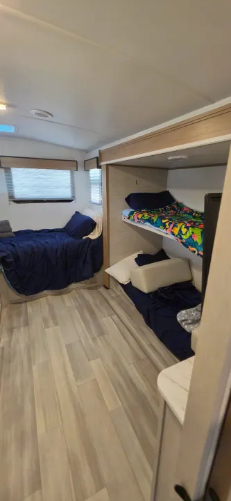 RV rental bedroom with a bed and bunk beds. Features light wood flooring and bright interior lighting.. Cruiser RV 2024