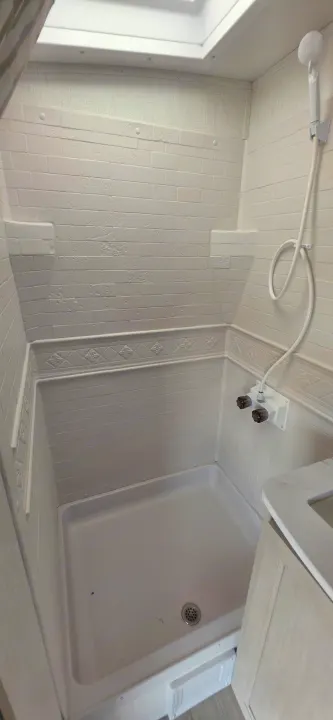 Clean, compact white RV rental shower with brick-patterned walls, ceiling vent, showerhead, and controls, ready for travel.. Cruiser RV 2024