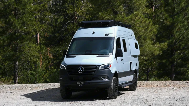 Adventure-ready white Mercedes Sprinter RV rental camper van on a gravel path against a pine forest backdrop.. Mercedes Winnebago 2026
