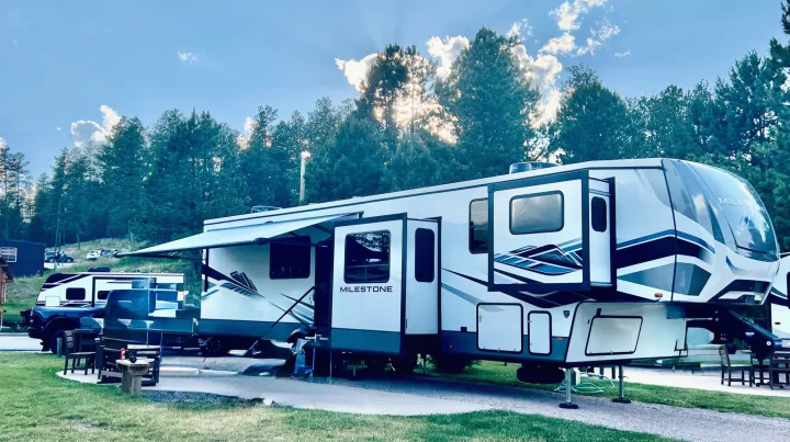 Milestone fifth-wheel rv rental with awning extended at a sunny, tree-lined campground under a blue sky.. Heartland RVs Milestone 2023