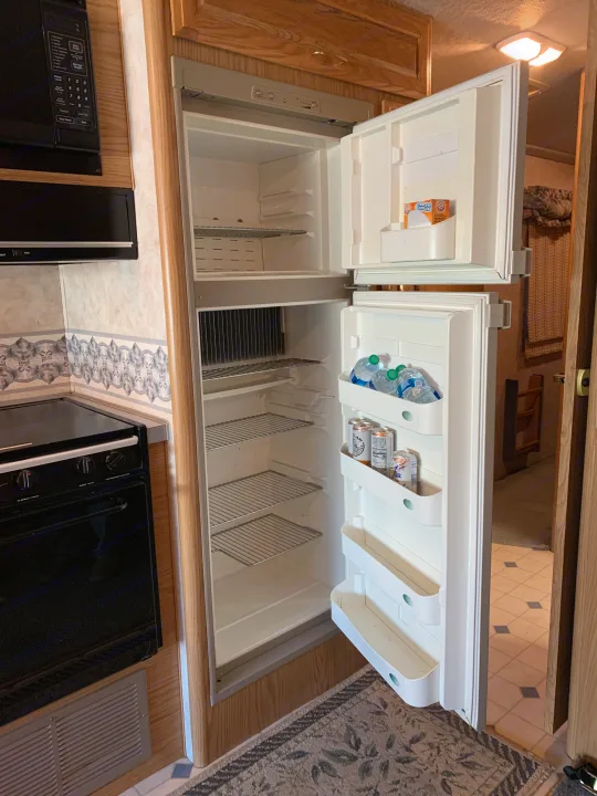 Inside an rv rental kitchen, an open refrigerator, microwave, and oven are visible. The fridge holds water, seltzer, and baking soda.. Fleetwood Bounder 1997