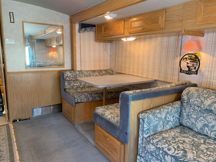 Cozy RV rental interior featuring a dinette with booth seating, a table, a patterned sofa, and light wood cabinetry.. Fleetwood Bounder 1997