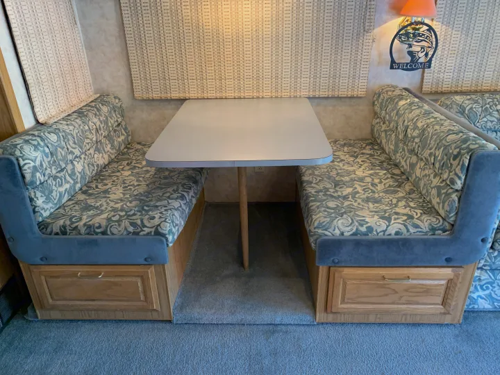 RV rental dinette: Two blue patterned benches face a light table, with wooden storage below. A cozy and functional interior.. Fleetwood Bounder 1997