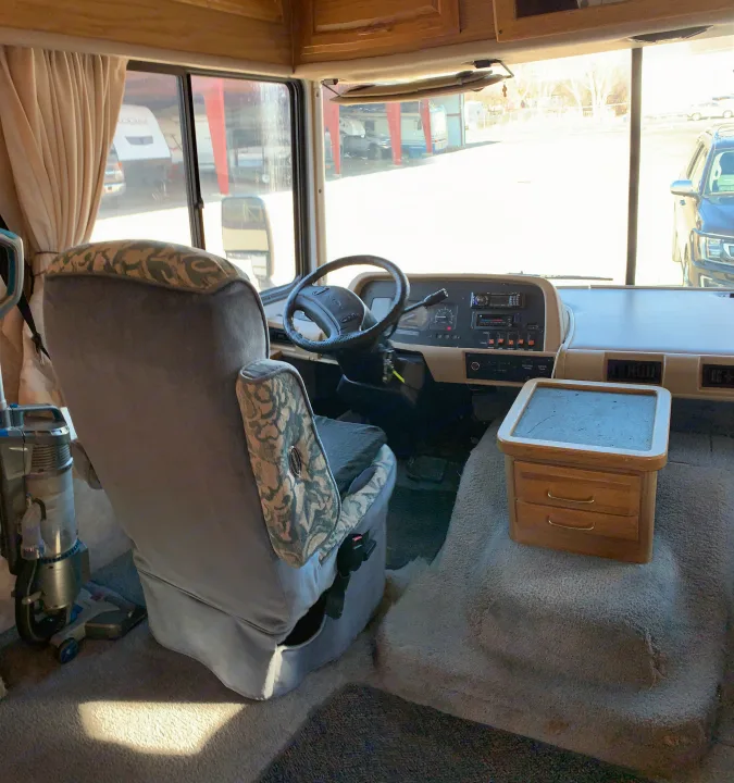 Interior view of an RV rental, showcasing the driver's seat, steering wheel, dashboard, and a small cabinet.. Fleetwood Bounder 1997