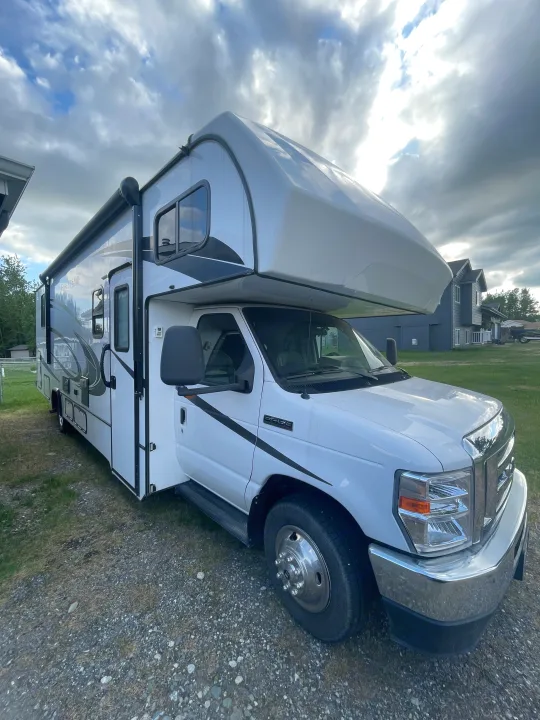 A white Class C rv rental, a motorhome with graphics, parked on gravel next to grass under a cloudy sky.. Forester LE 2022