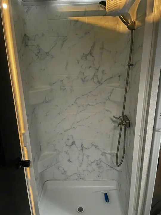 Modern, compact shower in an RV rental. Features marble-look walls, handheld shower, and a clean shower pan.. Forester LE 2022