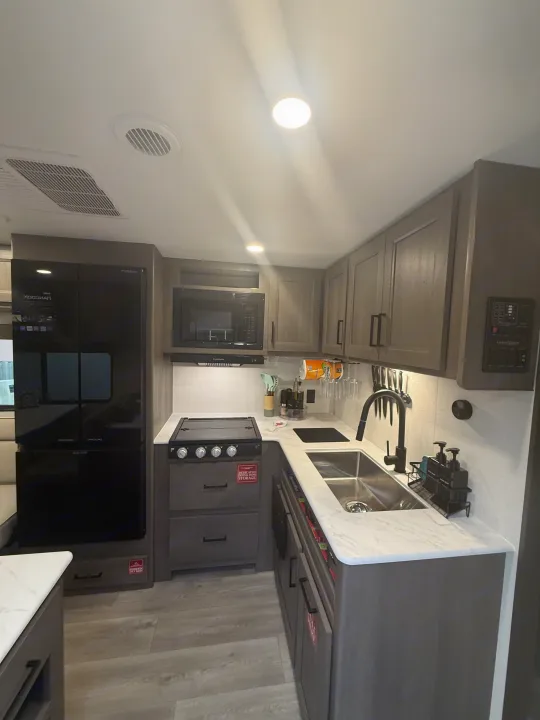 Explore this modern rv rental kitchen featuring a fridge, microwave, gas stove, and ample storage in a compact design.. Grand Design Transcend Xplor 2026