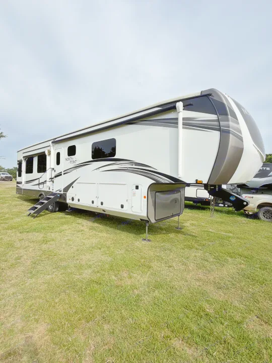 This white and gray North Point fifth-wheel RV, parked on grass under an overcast sky, is perfect for your next rv rental adventure.. Jayco North Point 2021