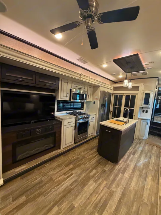 Modern rv rental interior: kitchen with island, stainless steel appliances, and living area with TV and electric fireplace.. Jayco North Point 2021