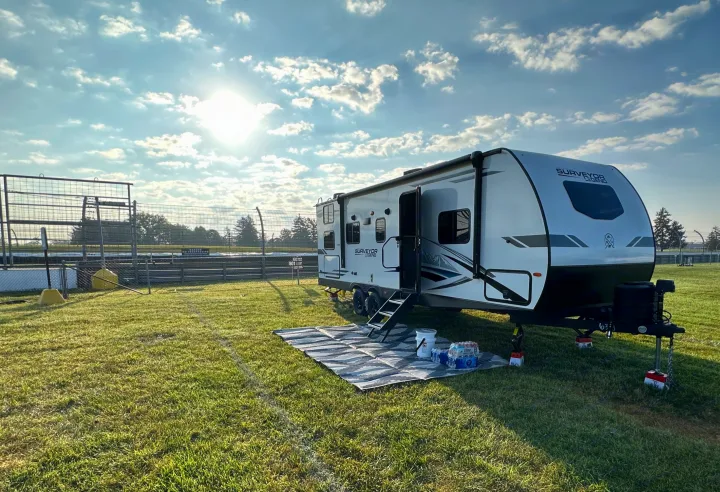 An RV rental, a Surveyor Legend travel trailer, parked on a sunny, grassy field next to a race track fence.. Forest River Surveyor Legend 2024