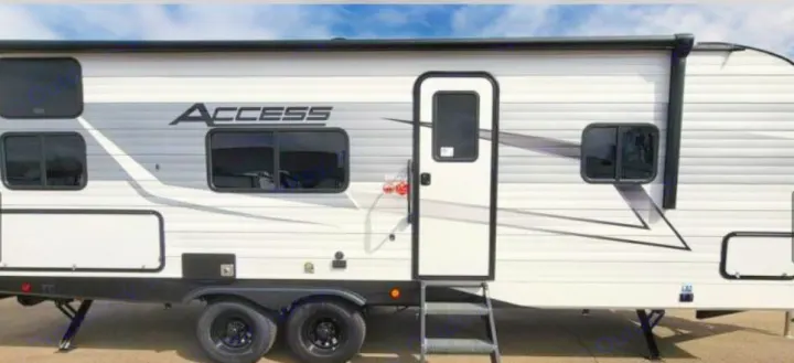 Side view of a modern white "ACCESS" travel trailer RV rental, featuring black trim, windows, and entry door with steps.. Winnebago Access 2025