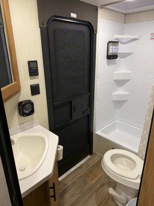 This RV rental bathroom offers a compact layout with a white sink, toilet, shower/tub combo, and utility controls.. Forest River Campsite reserve 26CJ 2025