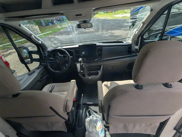 View inside an rv rental van, showing the front cabin. Features include a modern dashboard, large screen, steering wheel, and comfortable front seats with keys on one.. Coachmen Beyond 2023