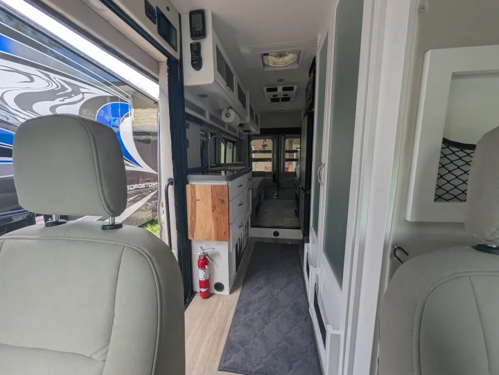 Inside this RV rental: front seats, galley kitchen with wood counter, hallway, and storage cabinets lead to the back.. Coachmen Beyond 2023