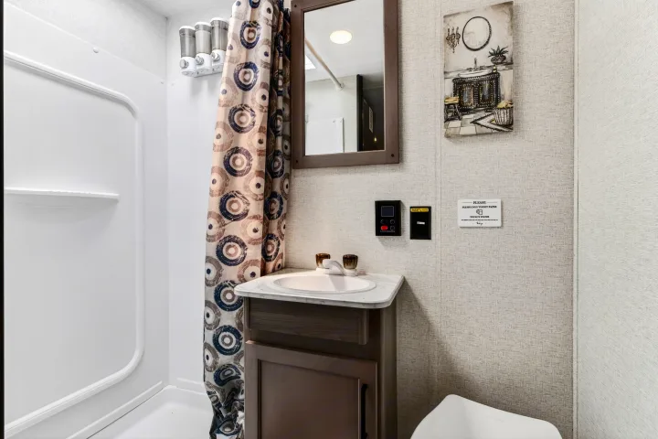 Compact RV rental bathroom showcasing shower, sink vanity, toilet, patterned curtain, and wall-mounted dispensers.. Keystone RV Hideout Sport 2024