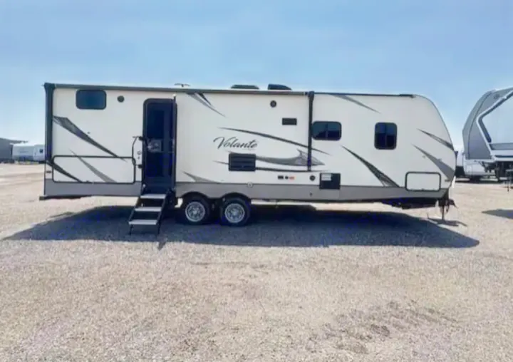 White Volante travel trailer for RV rental, parked on a sunny gravel lot with its entry door and steps open, ready for adventure.. Crossroads RV Volante 2019