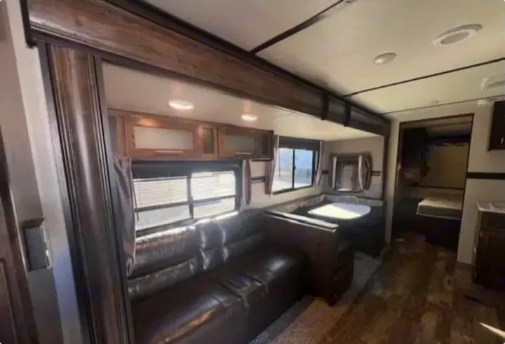 This inviting rv rental interior shows a dark leather sofa, dinette with table, overhead cabinets, and a back bedroom.. Crossroads RV Volante 2019