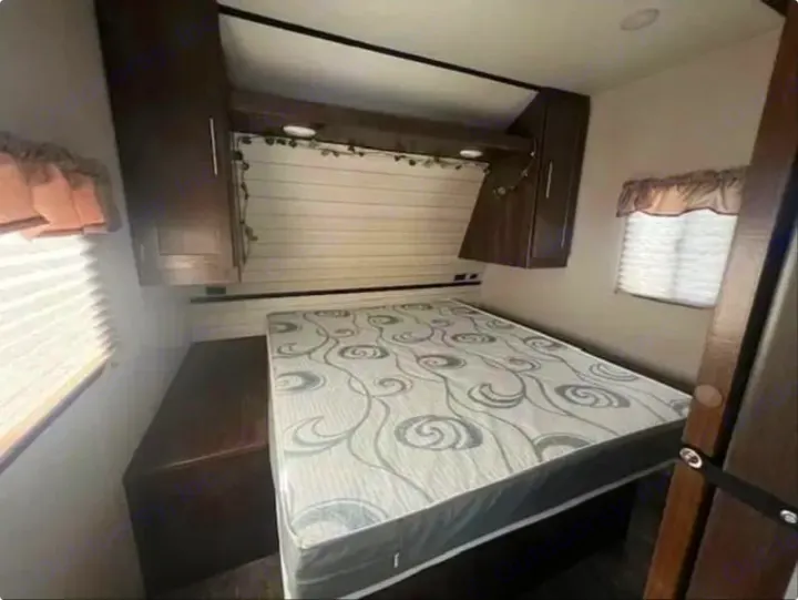 **RV rental** bedroom features a patterned mattress, overhead storage cabinets, and a window with blinds. Ideal for travel.. Crossroads RV Volante 2019