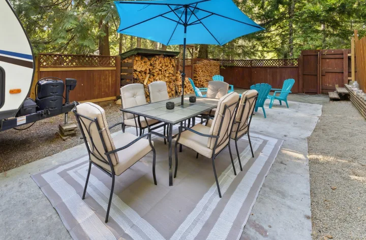 RV rental guests can enjoy this patio with a dining table, six chairs, and a blue umbrella, alongside the RV and a woodpile.. Crossroads RV Sunset Trail Super Lite 2022