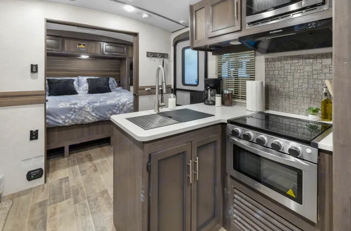 Inside an RV rental, a compact kitchen with a stove, oven, microwave, and sink, leading to a bedroom.. Crossroads RV Sunset Trail Super Lite 2022