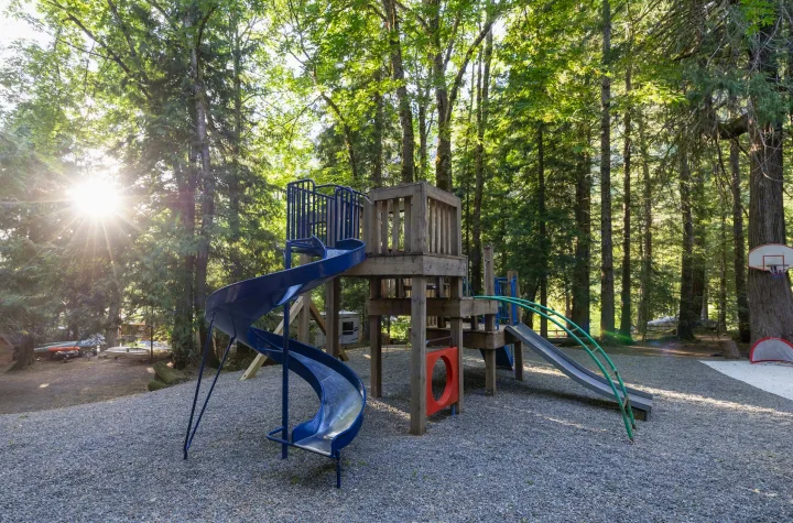 Wooded playground with slides, gravel ground & basketball hoop, perfect for family fun near your RV rental site.. Grand Design Imagine 2019