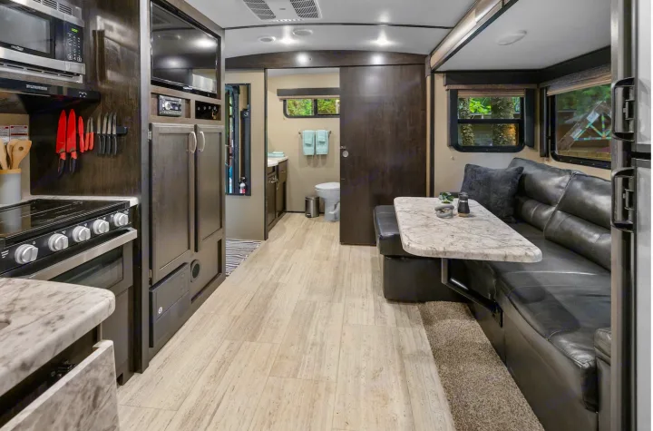 Modern RV rental interior: well-equipped kitchen, cozy dining booth, and bathroom with sliding door.. Grand Design Imagine 2019