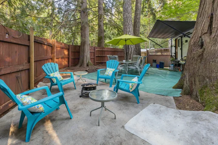 Enjoy this inviting RV rental patio featuring teal Adirondack chairs, fire pit, and dining space amidst tall trees.. Grand Design Imagine 2019