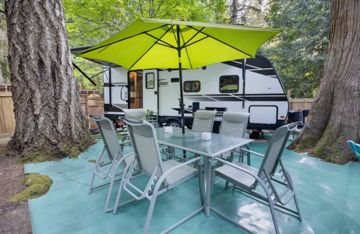 RV rental: Shaded outdoor patio with dining set & green umbrella next to a parked RV, offering a comfortable nature escape.. Grand Design Imagine 2019