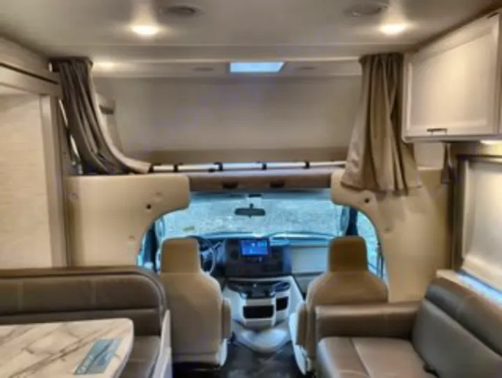 This inviting RV rental interior showcases the cockpit, overhead bunk, and a spacious living area with a dinette and sofa.. Thor Geneva 2025