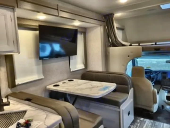 Inside this modern RV rental: a comfortable dinette with TV, cab-over bunk, and kitchen for travel ease.. Thor Geneva 2025